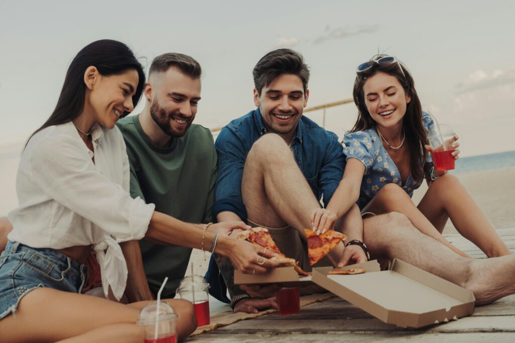 Happy young friends grabbing pizza while enjoying carefree time on the beach together